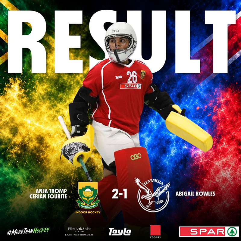 Result graphic for the third Test between South Africa and Namibia in the women's indoor hockey Test series, which South Africa won 2-1. South African goalkeeper Manisha Desai, wearing number 26 in a red playing kit with a white helmet, yellow gloves and red leg guards, stands in the centre of the frame. The word RESULT runs across the top in large white letters behind her. The background splits from green and gold smoke on the left, in the colours of the South African flag, to blue and red smoke on the right, in the colours of the Namibian flag. The South African indoor hockey crest and the Namibia hockey crest sit either side of the score, 2-1. The South African scorers, Anja Tromp and Cerian Fourie, are listed on the left, and the Namibian scorer, Abigail Rowles, on the right. A row of sponsor logos runs along the footer.